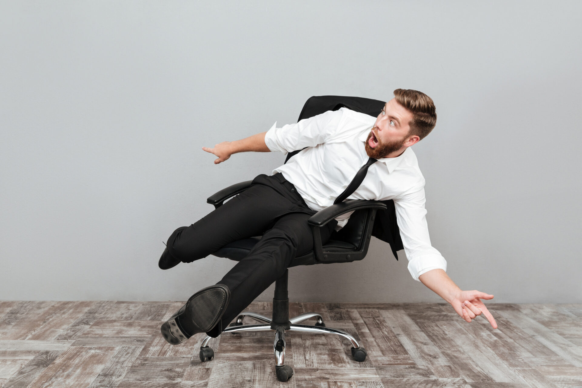 Funny crazy businessman having fun while sitting in office chair isolated over gray background